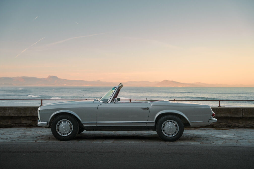 Classic Mercedes 280SL Pagoda parked by the sea at sunset, perfect for a vintage coastal road trip.