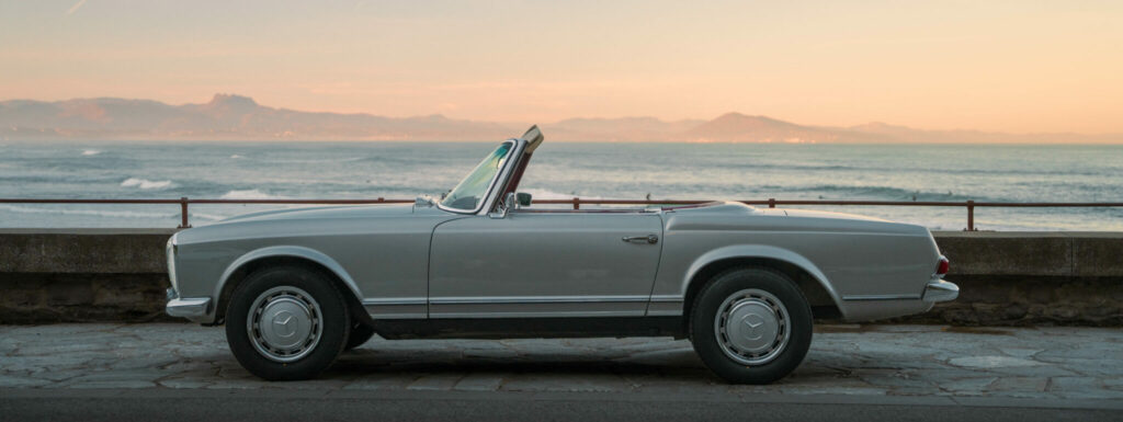 Classic Mercedes 280SL Pagoda parked by the sea at sunset, perfect for a vintage coastal road trip.