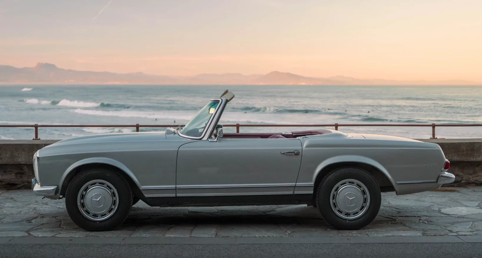 Classic Mercedes 280SL Pagoda parked by the sea at sunset, perfect for a vintage coastal road trip.