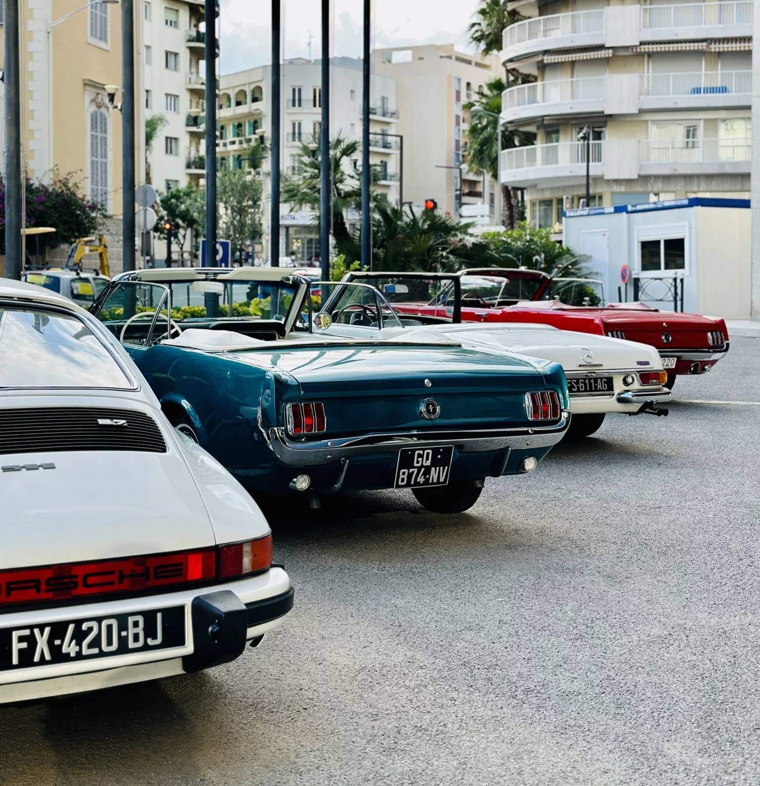 Rear view of a classic Porsche 911, Ford Mustang, and Mercedes Pagode convertible driving on a scenic road. Vintage car rally, Côte d'Azur.