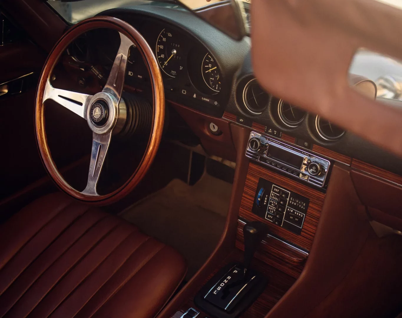 Refined interior of a vintage car with brown leather upholstery and wooden steering wheel, embodying the timeless style featured in 50' Inside.