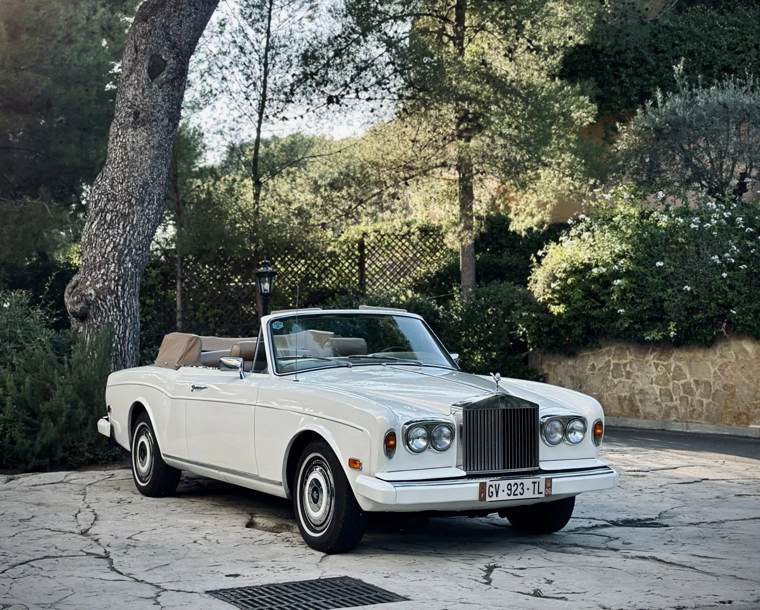 White 1978 Rolls-Royce Corniche parked on a paved driveway, surrounded by lush vegetation.